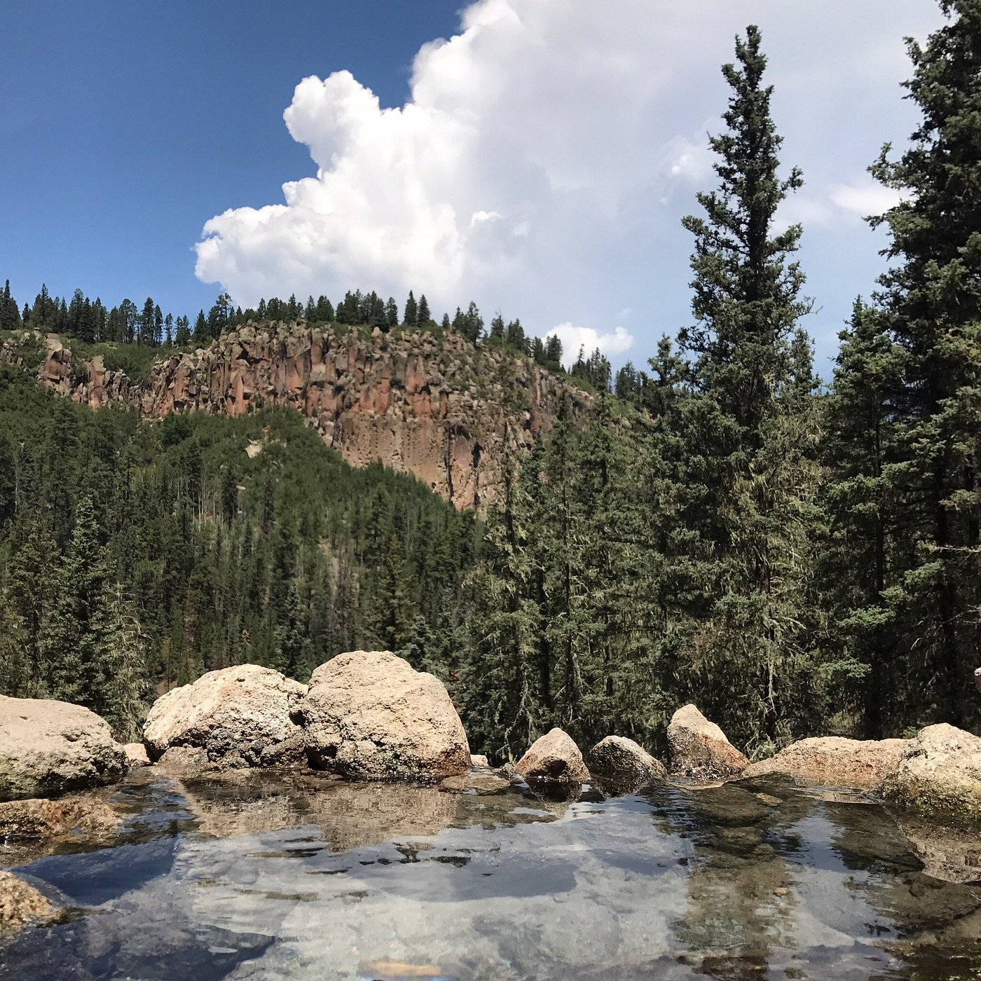 Natural hot spring pool surrounded by rocks and trees in Jemez Springs, New Mexico